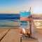 Woman holding seashell tumbler outdoors at table with an ocean view
